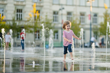 Wall Mural - Cute little boy having fun with water in city fountain. Child playing water games outdoors on hot day. Summer activities for children.