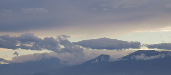 Wall Mural - Nuvole bianche e grigie aggrappate come ovatta alle montagne in una giornata invernale al tramonto