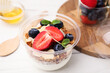 Tasty granola with berries, yogurt and almond flakes in plastic cup on white table, closeup