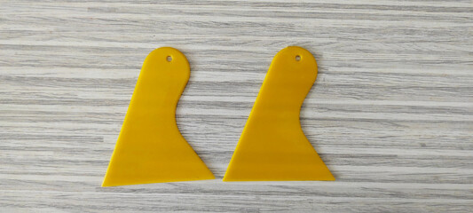 A pair of yellow paint scrapers which are very useful for smoothing cement, smoothing grout lines and covering cracks in isolated walls with a white wood pattern