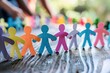 © Wan - Colorful paper cutouts of people holding hands on a wooden table, symbolizing unity, diversity, and community.