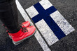 a woman with a boots standing on asphalt next to flag of Finland and border

