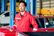 Asian machanician in red technical suit hold chart in car garage for service a car.