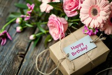 A Birthday Gift Box With Pink Flowers And A 'Happy Birthday' Tag On A Wooden Surface. Created With Generative AI