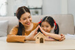 Cute little daughter and mother making symbolic roof of hands above home model together in living room. Safety and protection with love, care and security with happiness at home concept