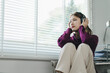 Depressed young woman with headphones sits in a chair and looking away at home.