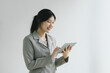 Confident Asian businesswoman smiling and using a digital tablet against a plain background.