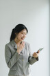 Confident Asian businesswoman smiling and using a digital tablet against a plain background.
