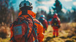© khonkangrua - Search and rescue team in bright orange uniforms equipped with backpacks walking through a forest.
