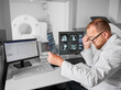 Medical computed tomography or MRI scanner. Side view of male doctor examining MRI results. Specialist wearing glasses and white robe, looking at x-ray, studying. Concept of medicine and healthcare.