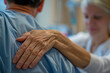 © xadartstudio - Close-up of a caregivers hand patting a patients shoulder, symbolizing empathy and support during recovery in a hospital environment