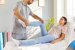 Physiotherapist treats leg injury and helps patient perform exercises for lower limbs. Female patient lies on medical couch in rehabilitation room and male doctor holds her foot and stretches her leg.