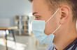 Side view close up portrait of pensive man doctor or nurse in blue face mask standing in medic office. Young male physician in clinic with copy space. Health care and medicine concept.
