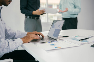 Fototapete - A man is typing on a laptop in front of a table with papers and a cell phone