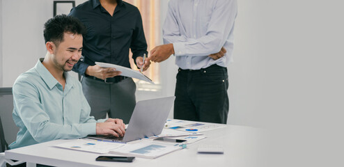 Wall Mural - A man is sitting at a desk with a laptop and a stack of papers