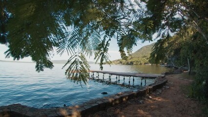 Wall Mural - Coast of the lake with wooden pier during calm sunny day