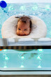 Small child or a baby is swimming and having a pleasant time during a physical therapy session in the pool. Baby is looking at camera and smiling.