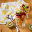 Healthy snack with chopped fruits and berries on the table. Tangerine, kiwi, banana, strawberries, mango, cherries and mint leaves in transparent cup