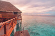 Perfect sunset on Maldives island, luxury water villas resort and wooden pier. Beautiful cloudy sky and beach background for summer vacation tourism travel vibes. Pristine sea water corals calm waves.