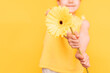 A little girl holding a yellow flower in front of her in front of her in front of a yellow background.