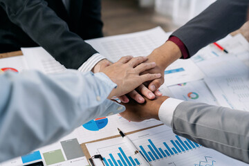 Wall Mural - A group of people are holding hands in a circle on a table with a lot of papers