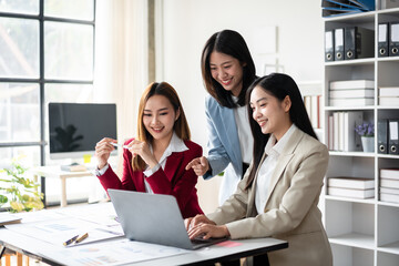 Three women are sitting at a desk with a laptop open