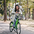 A woman is riding a green bicycle and looking at her phone