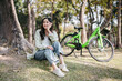 A woman is sitting on the grass next to a green bicycle