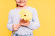 Child holding flower in her hands on Mother's Day holiday against yellow background.
