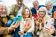 Group of senior people using technology devices together - Happy older friends having fun watching funny video on smartphone - Tech and modern elderly concept