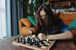 © SHOTPRIME STUDIO - Woman enjoying a game of chess on a wooden board in a cozy living room setting