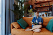 © SHOTPRIME STUDIO - Woman relaxing on orange couch near window reading book in cozy living room with daylight shining through