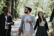 © qunica.com - A cheerful group of multiracial friends laughs and chats as they walk through a sunny, tree-lined urban park, embodying joy and togetherness.