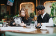 Two young business professionals collaborate using a digital tablet in a cafe setting, indicating teamwork, technology, and modern work culture.