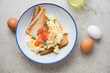 Toasts with scrambled eggs and smoked salmon in a blue and white plate, top view on a beige stone background, horizontal shot