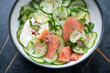 Bowl of cucumber salad with smoked salmon and poached egg, horizontal shot on a dark-green marble surface, middle closeup