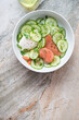 White bowl with smoked salmon and cucumber salad, top view on a grey and roseate granite background, vertical shot, copy space