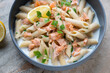 Penne pasta with salmon flakes served in a grey bowl, horizontal shot, middle close-up