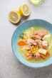 Chowder with salmon served in a turquoise bowl on a beige stone background, vertical shot, elevated view, selective focus