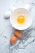 Bowl with uncooked goose and raw chicken eggs on a white marble background, vertical shot, above view
