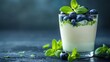   A glass of yogurt topped with blueberries and mint sits amidst leaves