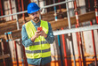 © Mediteraneo - Construction site manager standing  wearing safety vest and helmet, using his phone at construction site.