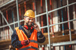 © Mediteraneo - Construction site manager standing  wearing safety vest and helmet, talking to the phone at construction site.