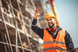 © Mediteraneo - Construction site manager standing  wearing safety vest and helmet, thinking at construction site. Young architect watching construction site with confidence. Waving at someone
