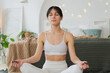 Yoga mindfulness meditation. Young healthy woman practicing yoga in living room at home. Woman sitting in lotus pose meditating smiling relaxing indoor. Girl doing breathing practice. Yoga at home