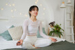 Yoga mindfulness meditation. Young healthy woman practicing yoga in bedroom at home. Woman sitting in lotus pose on bed meditating smiling relaxing indoor. Girl doing breathing practice. Yoga at home