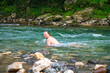 Man with Long Hair Immersed in Nature Swimming in a Mountain River Amidst Trees and Rocks