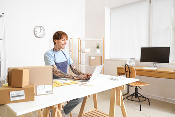 Wall Mural - Young online store seller working with laptop at table in warehouse