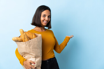 Poster - Young latin woman buying some breads isolated on blue background extending hands to the side for inviting to come