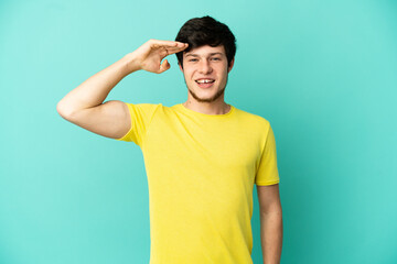 Wall Mural - Young Russian man isolated on blue background saluting with hand with happy expression